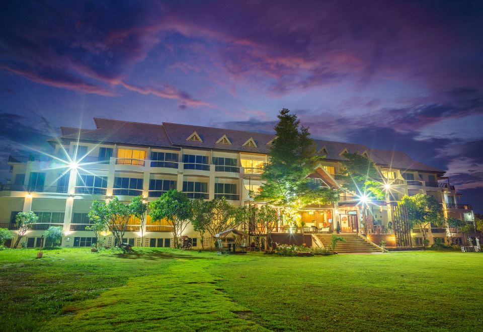 a large building surrounded by a grassy field , with trees and lights illuminating the scene at night at Vieng Khong Hotel