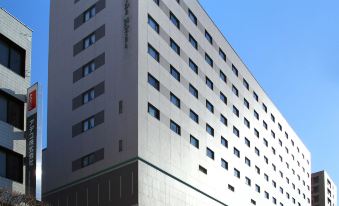 a large , modern building with multiple floors and windows , situated in a bustling city street at Numazu River Side Hotel