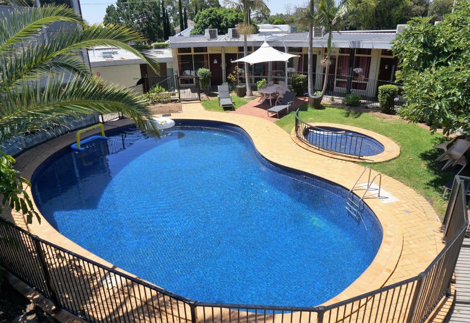 a large , blue swimming pool surrounded by a patio area with chairs and umbrellas , situated next to a building at Jacksons Motor Inn