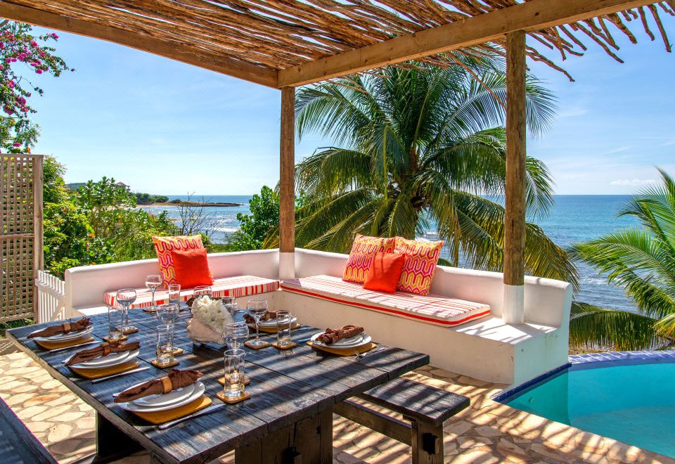 a table with plates and silverware is set on a patio overlooking the ocean , with a view of palm trees in the background at Hope House