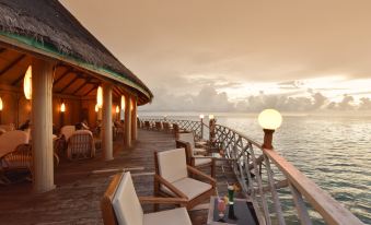 a wooden deck overlooking the ocean , with several chairs and a table set up for outdoor dining at Angaga Island Resort & Spa