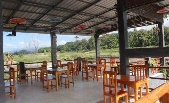 an empty outdoor dining area with wooden tables and chairs under a metal roof , overlooking a lush green field at Peisanae Faikeng Resort