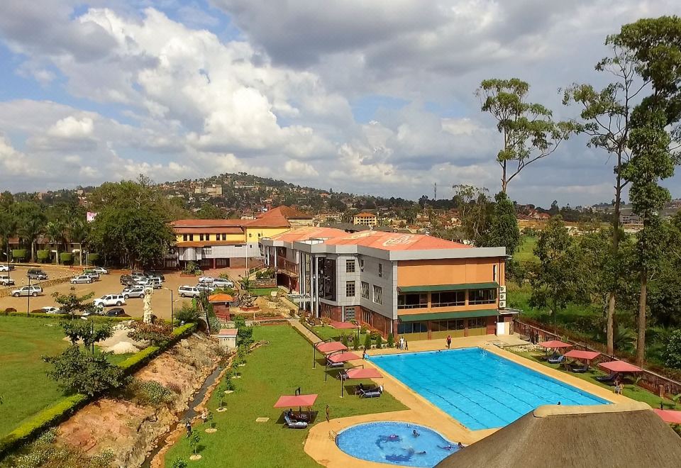 a large swimming pool is surrounded by a building with a red roof , surrounded by trees and other buildings in the background at Silver Springs Hotel Uganda