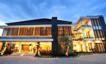 a modern , two - story building with a stone wall and large windows at night , surrounded by trees and a paved walkway at Kautaman Hotel