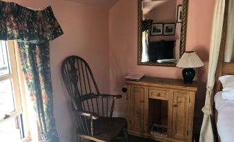 a wooden chair and a lamp are placed in a room with pink walls , a window , and a mirror at Cross Keys