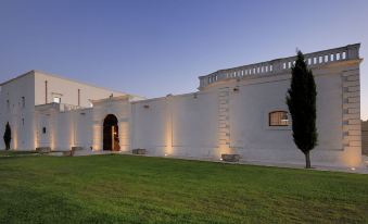 a large white building with a green lawn in front of it , surrounded by trees at Masseria Amastuola Wine Resort