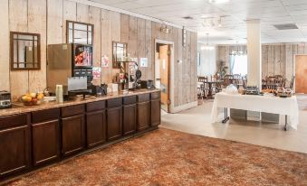 a dining area with a long wooden table and chairs , as well as a kitchen counter with various appliances at Rodeway Inn