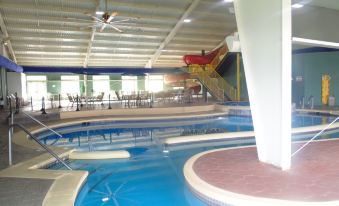an indoor swimming pool with a water slide , surrounded by chairs and tables for dining at Lakeside Resort & Conference Center