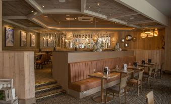 a restaurant with wooden tables and chairs , a bar in the background , and lights hanging from the ceiling at Riverside Lodge Hotel