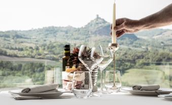 a person is holding a lit candle next to a table with wine glasses , bottles , and other items on it at Albergo Posta Marcucci