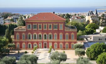 an aerial view of a red brick building with columns and a courtyard surrounded by trees , overlooking the ocean at Splendid Hotel & Spa Nice