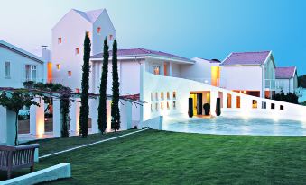 a white building with a green lawn in front of it , and tall trees on either side of the yard at La Coluccia