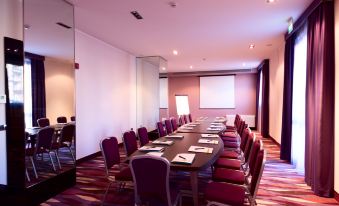 a long conference table with chairs is set up in a conference room with pink walls and a screen at Quality Hotel Green Palace