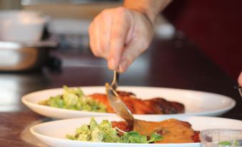 a person is using a spoon to serve food on plates , which appear to be prepared for a meal at Rioshouse George-Inn
