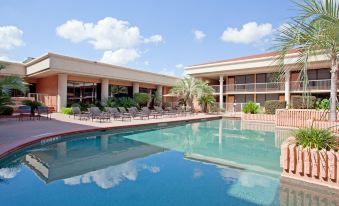 a large outdoor pool surrounded by several lounge chairs and tables , with a building in the background at Holiday Home Park Central Port Arthur