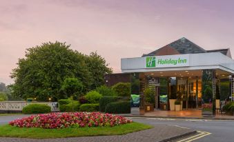 a holiday inn building with a large sign above the entrance , surrounded by flowers and trees at Holiday Inn Leeds - Garforth