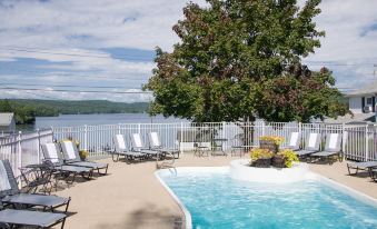 a large pool surrounded by lounge chairs and umbrellas , with a view of the lake in the background at Lake Bomoseen Lodge