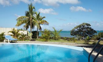 a large blue pool is surrounded by palm trees and overlooks the ocean , with palm trees in the foreground at Flowers of Paradise with Lov
