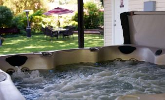 a hot tub filled with water is seen in the foreground , while an outdoor dining area and umbrellas can be seen in the background at Fiddler's Inn