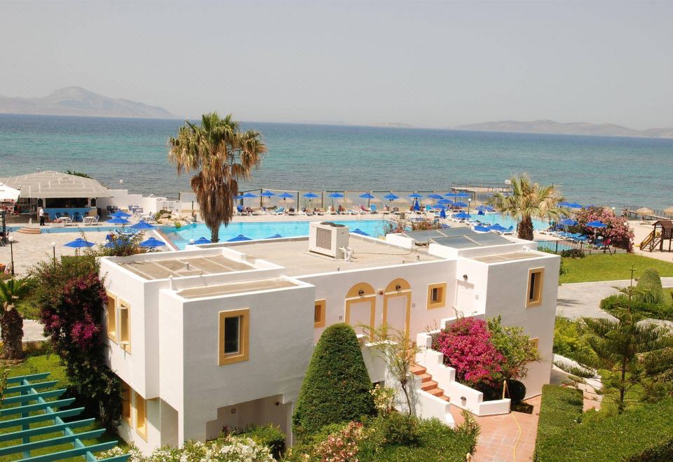 a large white house with a pool in the front yard , surrounded by palm trees and overlooking the ocean at Mastichari Bay Hotel