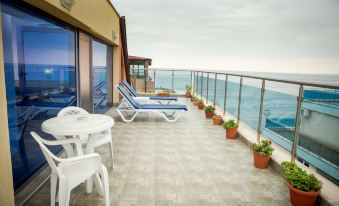 a balcony with white chairs and tables , overlooking the ocean , under a cloudy sky , and several potted plants in pots at Hotel Bijou