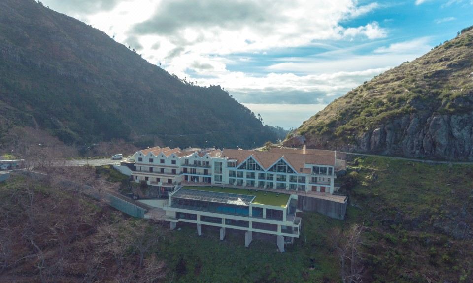 a large building with a green roof is situated on a hillside overlooking the ocean at Eira do Serrado - Hotel & Spa