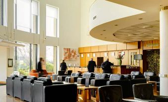 a hotel lobby with several couches , chairs , and a reception desk , as well as people standing or sitting in the background at Maldron Hotel Belfast International Airport