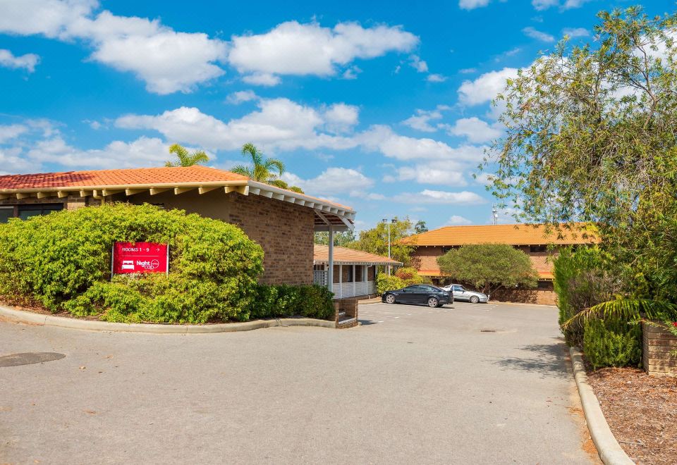 a brick building with a red sign and palm trees in front of it , under a blue sky with white clouds at Nightcap at Wanneroo Tavern