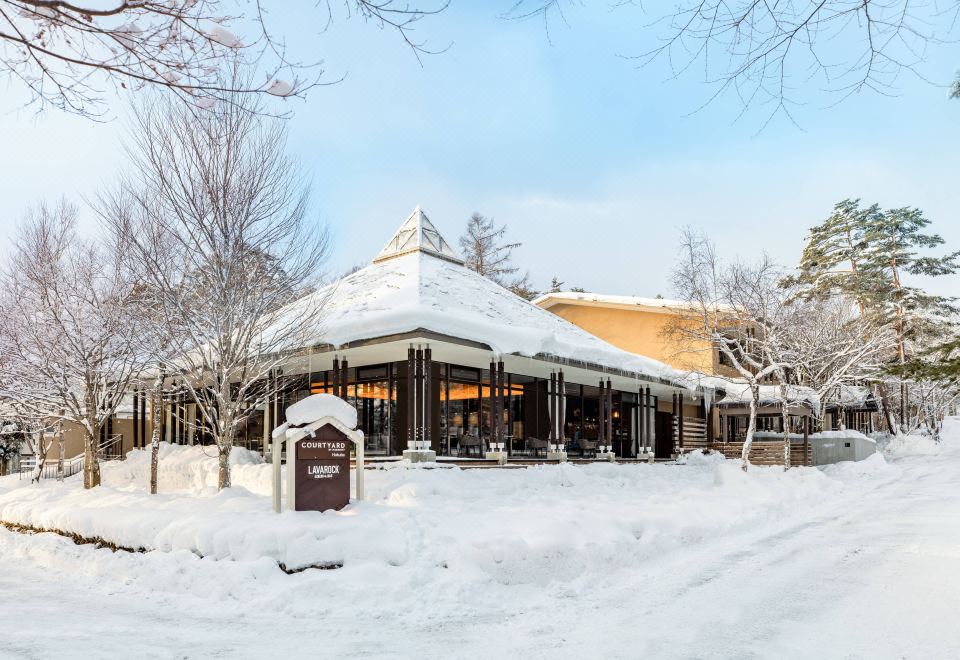 a large wooden building surrounded by snow - covered trees and bushes , creating a serene winter scene at Courtyard by Marriott Hakuba