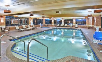 a large swimming pool with a diving board and lounge chairs is surrounded by pillars at Holiday Inn Manitowoc
