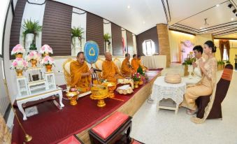 a group of monks in orange robes sitting on a throne in a room with white chairs and flowers at Lampam Resort