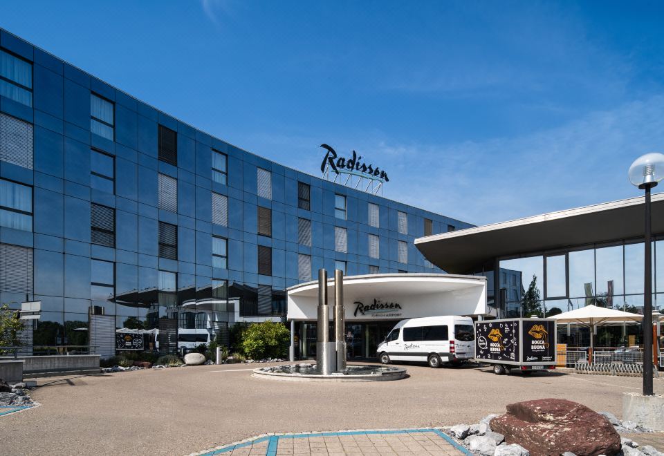 a large hotel building with a parking lot in front of it , where a parking lot is occupied by cars at Radisson Hotel Zurich Airport