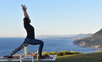 a woman is doing a yoga pose on top of a hill with a view of the ocean at Heart & Soul Retreats
