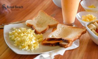a wooden dining table with a plate of scrambled eggs , toast , and a glass of orange juice at Royal Beach
