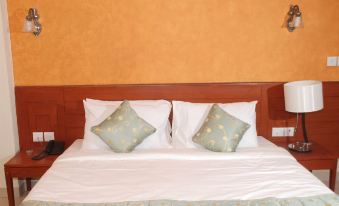 a neatly made bed with two pillows and a white comforter , set against an orange wall at Sun City Resort