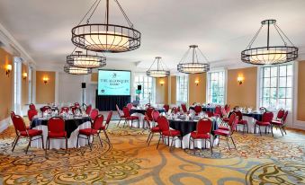 a large conference room with multiple tables and chairs , a projector screen , and hanging lights at The Algonquin Resort St. Andrews by-The-Sea, Autograph Collection