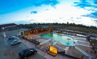 a large swimming pool with a fountain and a yellow structure in the background , surrounded by trees and buildings at Sukhothai Porncharoen Resort & Spa