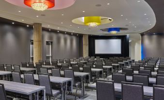 a large , empty conference room with rows of chairs and tables , a projector screen , and colorful pendant lights at Aloft Richardson