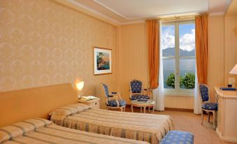 a hotel room with two beds , a window offering a view of the mountains , and various furniture items at Grand Hotel Menaggio