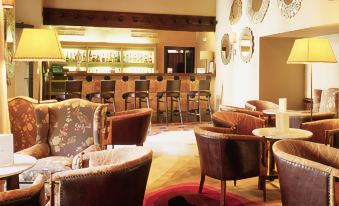 a well - decorated bar area in a hotel , with several chairs and tables arranged for patrons to enjoy drinks and socialize at Parador de Zafra