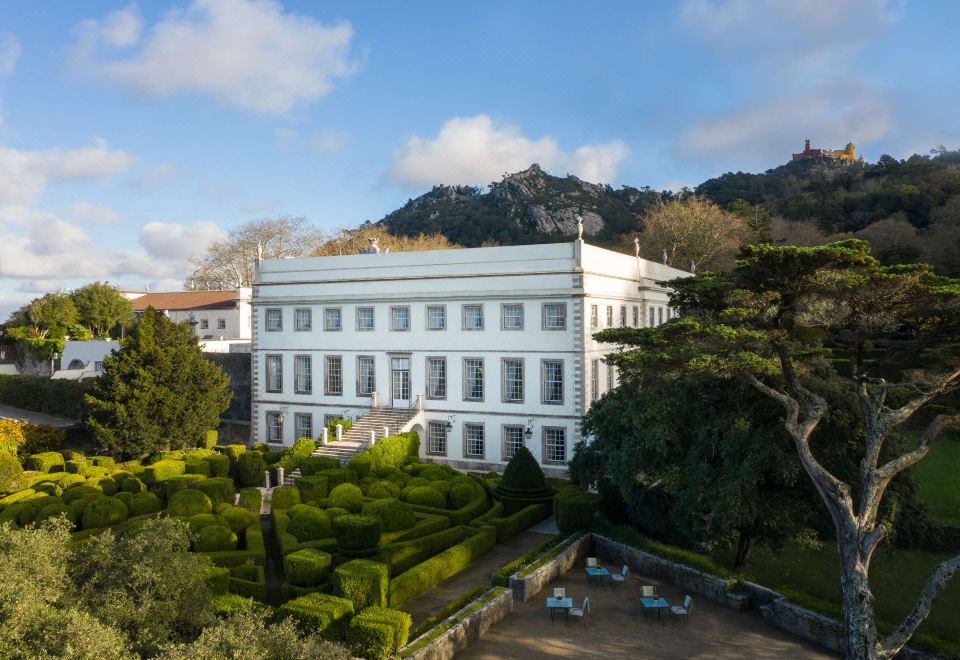 a large white building surrounded by trees and bushes , with a mountain in the background at Valverde Sintra Palácio de Seteais