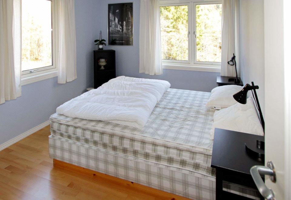 a neatly made bed with white sheets and pillows in a bedroom with wooden flooring , near two windows at Lindesnes