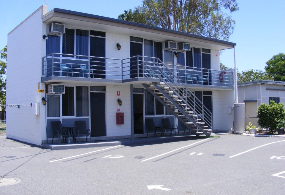 a two - story building with a staircase leading to the second floor , surrounded by trees and a parking lot at Motel Lodge