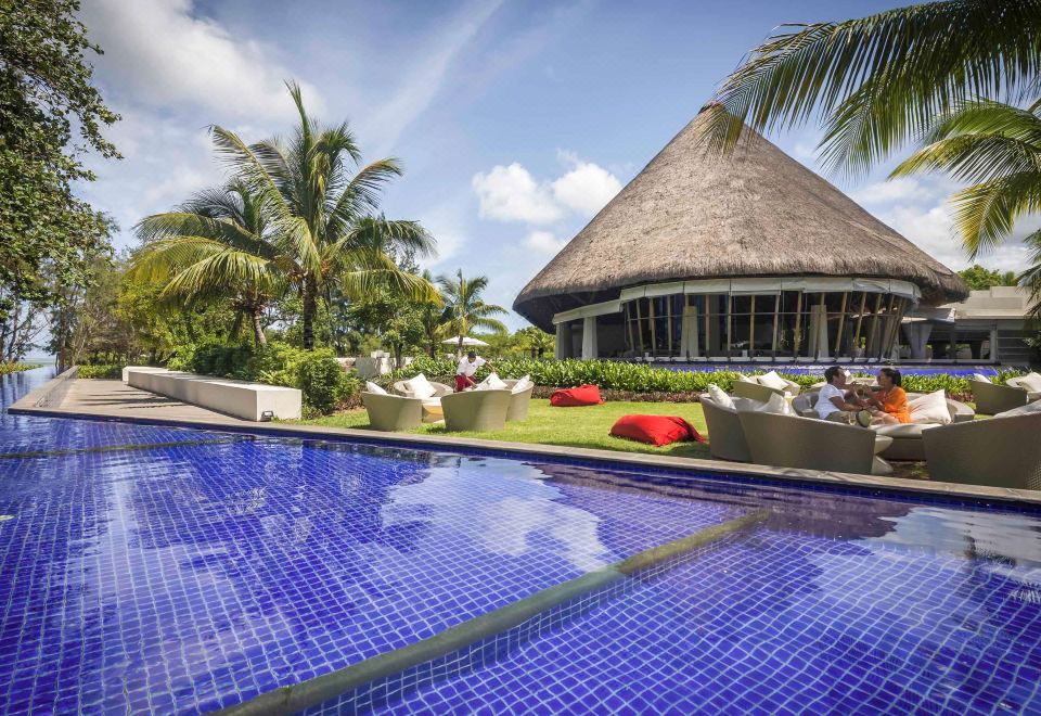 a resort with a large pool surrounded by lounge chairs and palm trees , creating a relaxing atmosphere at SO Sofitel Mauritius
