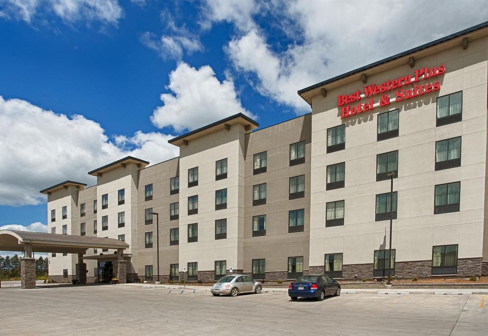 a large hotel with a red sign on the side , located in a city setting at Best Western Plus Williston Hotel  Suites