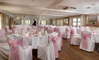 a large banquet hall filled with tables and chairs , all covered in white tablecloths and adorned with pink ribbons at Best Western Ivy Hill Hotel