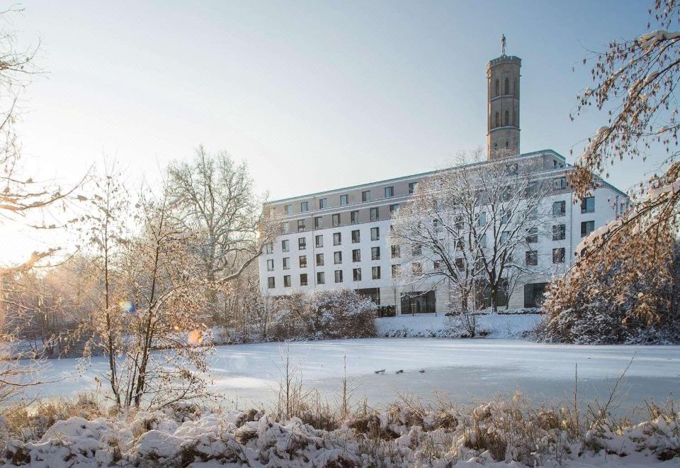 a large white building surrounded by snow - covered trees and a frozen lake , creating a picturesque winter scene at Steigenberger Braunschweig