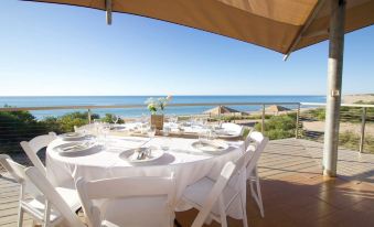 a white dining table with chairs is set up on a balcony overlooking the ocean at Eco Beach Wilderness Retreat