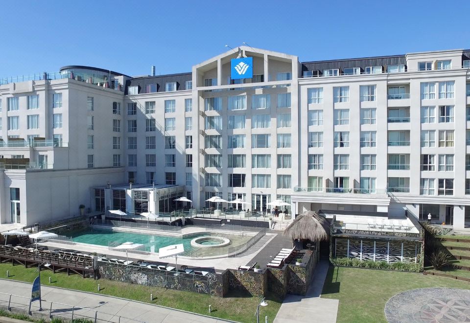 a large hotel with a pool and a fountain in front of it , surrounded by grass at Wyndham Nordelta Tigre Buenos Aires