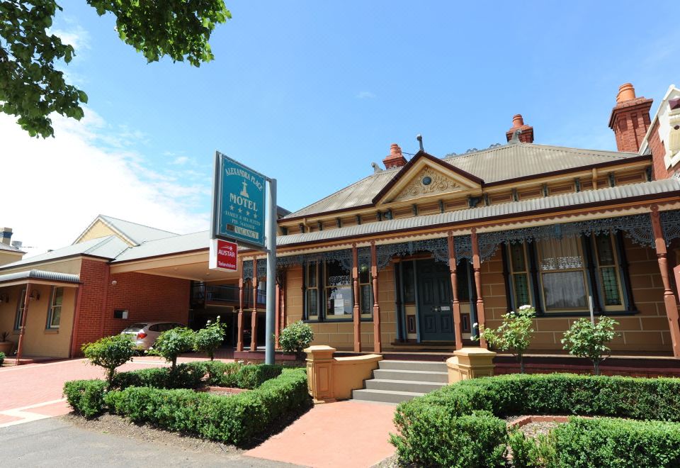 a brick building with a green sign on the front , surrounded by trees and bushes at Alexandra Place